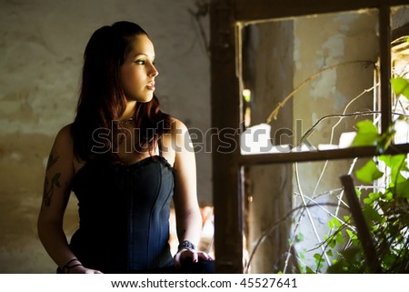 Young beautiful goth girl looking at broken window.