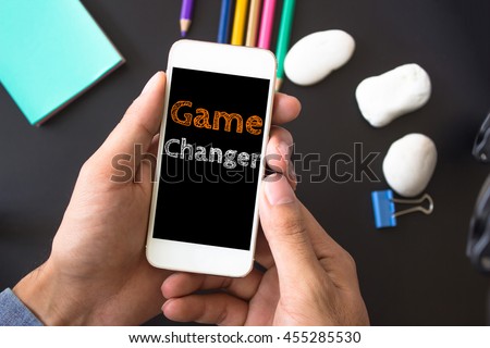 Game changer, text message on screen at hands take smartphone, black table with office supplies backdrop background . business concept.
