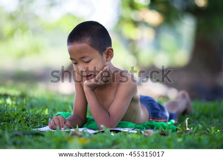 Little asia boy reading a book under big tree in countryside.