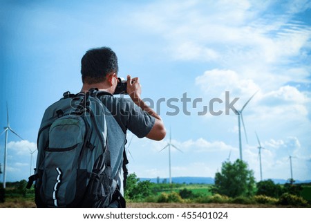 A man asia with backpack taking a photo on view of the wind turbine .