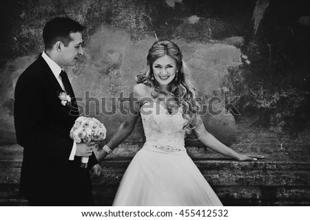 Blck and white picture of stunning bride leaning on old wall behind a groom