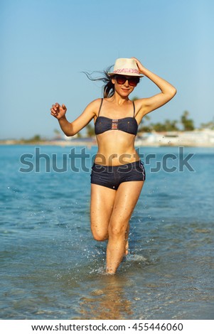 Beach vacation. Young woman in a hat and swimsuit walking on the beach on a hot summer day