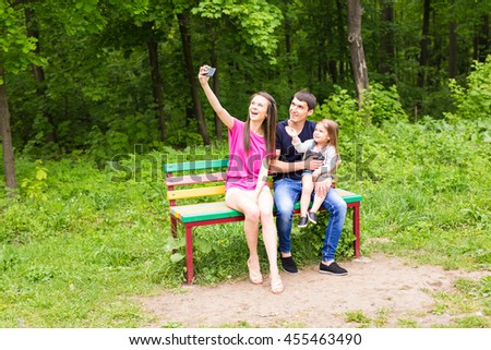 Summer scene of Happy young family taking selfies with her smartphone in the park