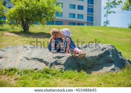 Toddlers Boy and girl kissing in summer park on a large rock