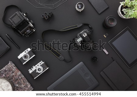 Work space on black table of a creative designer or photographer with laptop, tablet, cameras other objects of inspiration and copy space. Stylish home studio concept of technology trends.