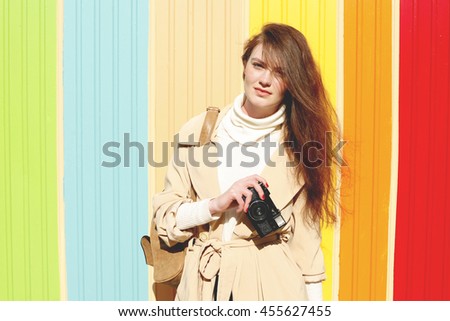 Woman photographer takes images with retro camera. Pretty female student wearing a beige trench coat with leather backpack traveling on European streets on a sunny day . Autumn fashion