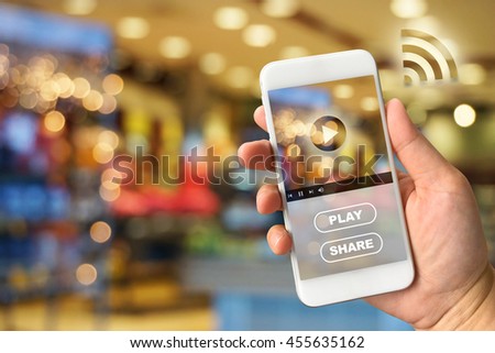 Woman hand holding smartphone against blur bokeh of shop background VDO ads concept Royalty-Free Stock Photo #455635162