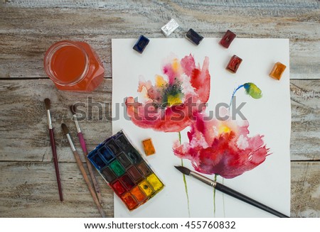 Watercolor paints, brushes and painted flowers on wooden background. The workplace of the artist.