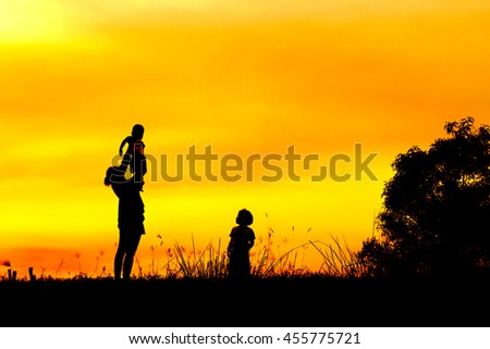 A silhouette of a happy young mother, laughing as she plays with her toddler child and lifts him over her head outside on During sunset