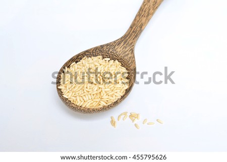 Uncooked brown rice in a wooden spoon, white background