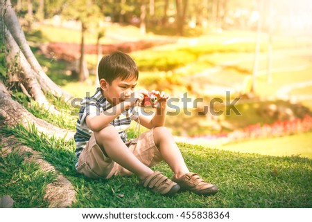 Serious asian boy trying to take photo by camera on nature background. Child relaxing outdoors in the day time at park, travel on vacation. Positive human emotion.