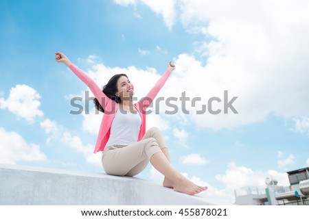 Freedom concept. Enjoyment. Asian young woman relaxing under blue sky on rooftop with her hands raised towards sky Royalty-Free Stock Photo #455878021