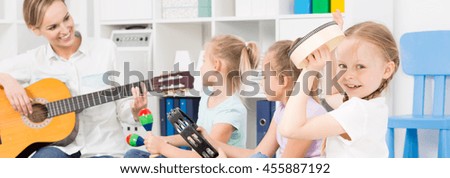 Young woman playing the guitar close to the three girls with tambourines with the case full of toys behind them