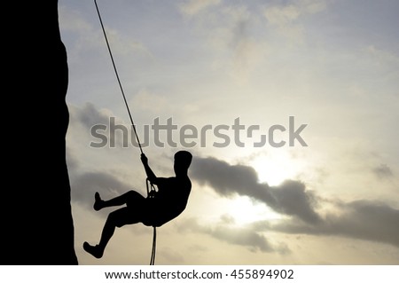 Silhouette of young man abseiling down from a cliff, sun, beautiful colorful sky and clouds behind. Climber rappelling from a rock.