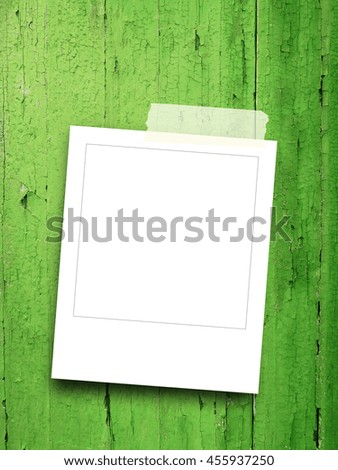 Close-up detail of one blank square instant photo frame with adhesive tape on green wooden boards background