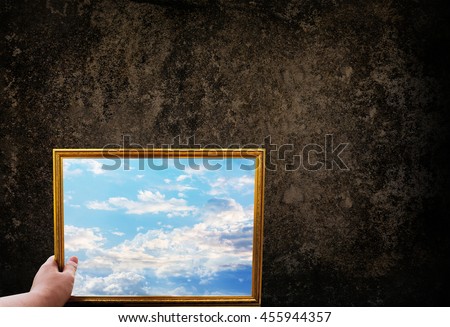 Hand hold picture frame of wide puffy cloud sky on dark grunge wall