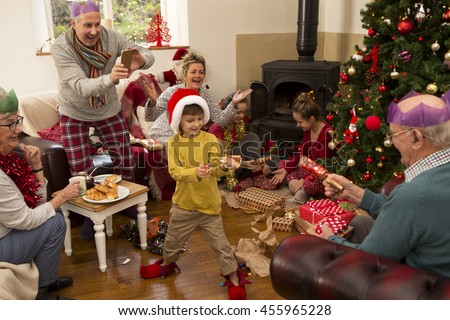 A family are sat around a christmas tree, opening presents and pulling crackers.