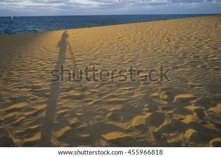 Golden sand shadow/Long shadow of photographer and tripod on a golden sand dune with the sea and sky at the horizon at sunset.