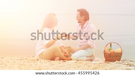 Summer, holidays, vacation and happy people concepts. Toned picture of happy couple having picnic, they are drinking red wine and sitting at beach.