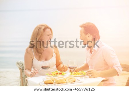 Toned picture of beautiful couple resting in restaurant or cafe by sea. Handsome man and beautiful woman having lunch or dinner with delicious red wine.