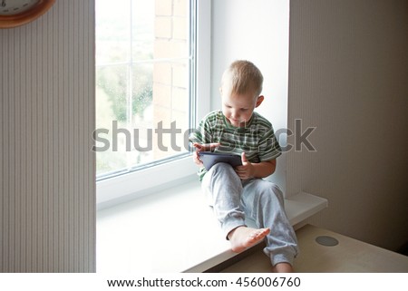 boy home sits on the window sill in the green shirt and the pants play looks tablet cartoons games movies movie