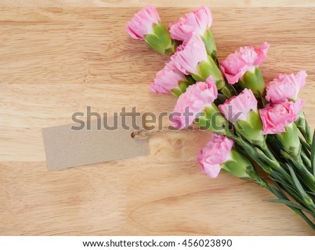 Brown blank label and bouquet pink Carnation flower on wood background (top view)