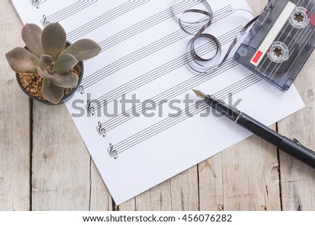 Sheet music, cactus, fountain pen, tape cassette on wooden table, flat lay