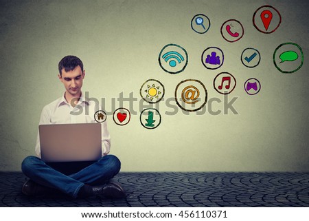 Young man working using laptop sitting on a floor social media application icons flying up. Modern communication technology concept