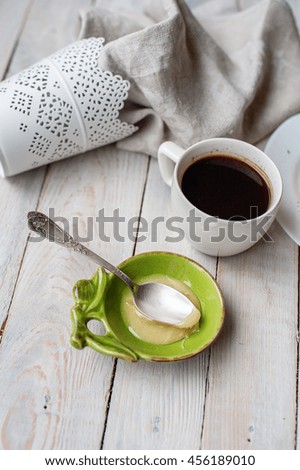 honey into a bowl of olive color and black coffee in a white cup on a light wooden background