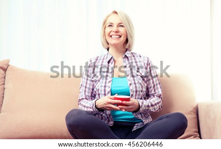 Happy relaxed woman sitting and dreaming on the sofa in the living room with cup of coffee. By toning applied photo