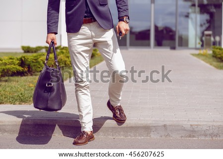 fashionably dressed businessman walks from office building with a bag and car keys in his hand. Royalty-Free Stock Photo #456207625
