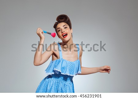 Picture of beautiful pin-up girl at studio holding make-up brush