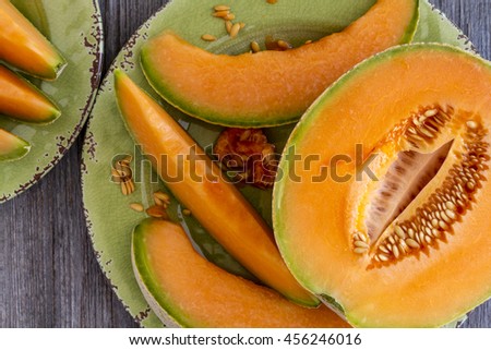 Close up of cut open cantaloupe melon half and slices sitting on green rustic plate on wooden tabletop