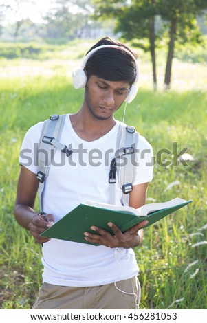 indian college male student using book and phone outdoor