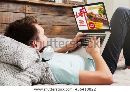 Man ordering take away food by internet with a laptop while lying at home. Royalty-Free Stock Photo #456418822