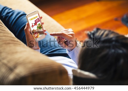 Woman ordering take away food by internet with a mobile phone while lying down at home.