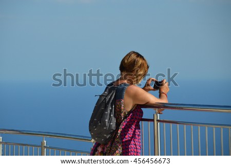 Female solo traveller takes a picture with her smartphone at panorama point in Dubrovnik. Blue sky merges with the blue sea. Lots of copy space.