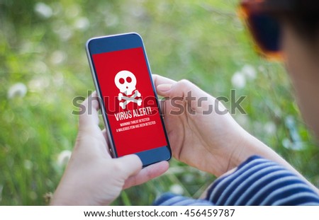 girl in the grass holding her smartphone showing virus alert. All screen graphics are made up.