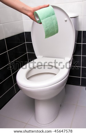Human hand holding green toilet paper on the background of toilet bowl