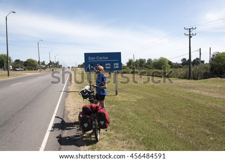 Man standing with a full loaded folding bicycle at the entrance to San Carlos city,Uruguay