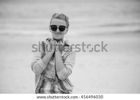 advertisement, summer holidays, travel and people concept - happy smiling young attractive girl in jeans and glasses posing on the beach on a background of the sea. Smile and happy face.