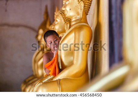 Young Novice monk scrubbing buddha statue at temple in thailand