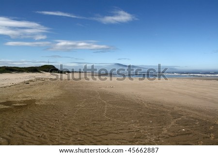 blue sky with clouds under the broad sandy seashore in the day-time in summer, sea in the distance