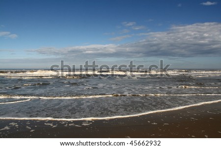 blue sky with clouds and broad waves on the sandy seashore in the day-time in summer