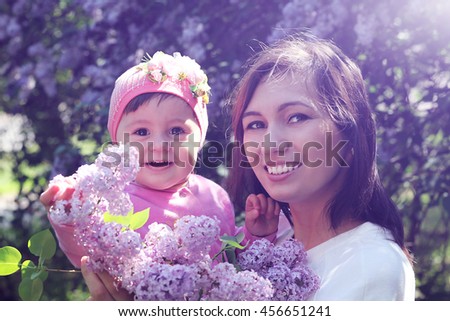 Young mother with a small child in her arms in nature with flowers lilac. Instagram effect, toned photo filter