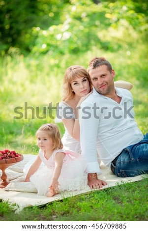 Beautiful pregnant woman with her husband and young daughter in green garden