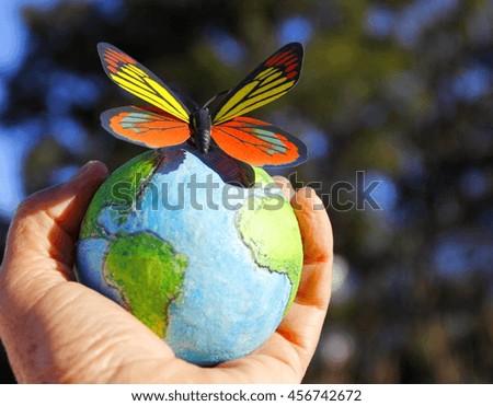 Butterfly over earth globe. Hand with a handmade earth globe and a butterfly on blurred natural background.