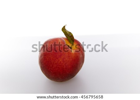 one ripe peach red with one green leaf on a light background