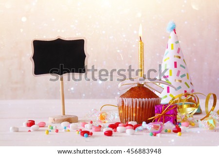 Birthday concept with cupcake and candle next to little chalkboard on wooden table. Glitter overlay