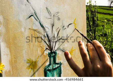 Young female artist painting flowers in bottle on canvas in summer field